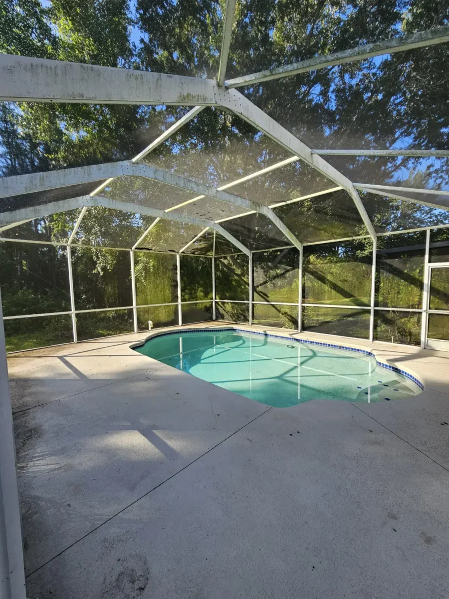 Let Us Restore Your Outdoor Living Space Small outdoor swimming pool with a protective screened enclosure surrounded by a concrete deck and greenery