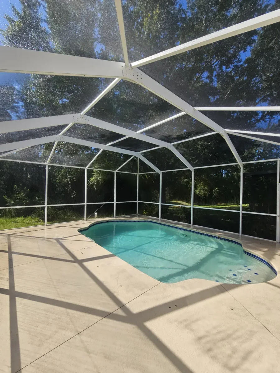 Let Us Restore Your Outdoor Living Space Small outdoor swimming pool with a protective screened enclosure surrounded by a concrete deck and greenery