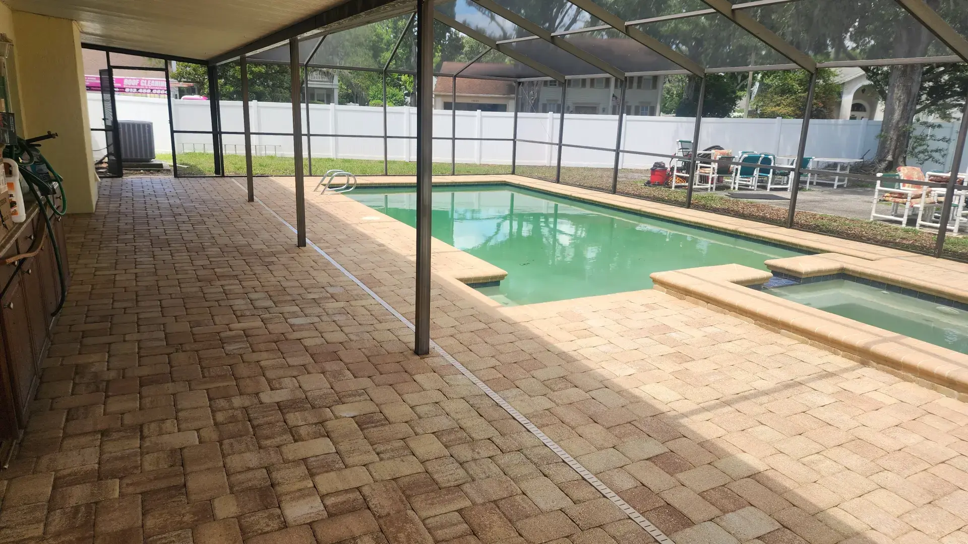 Let Us Restore Your Outdoor Living Space Spacious screened-in outdoor pool area with beige brick paver flooring and adjacent hot tub under shade structure