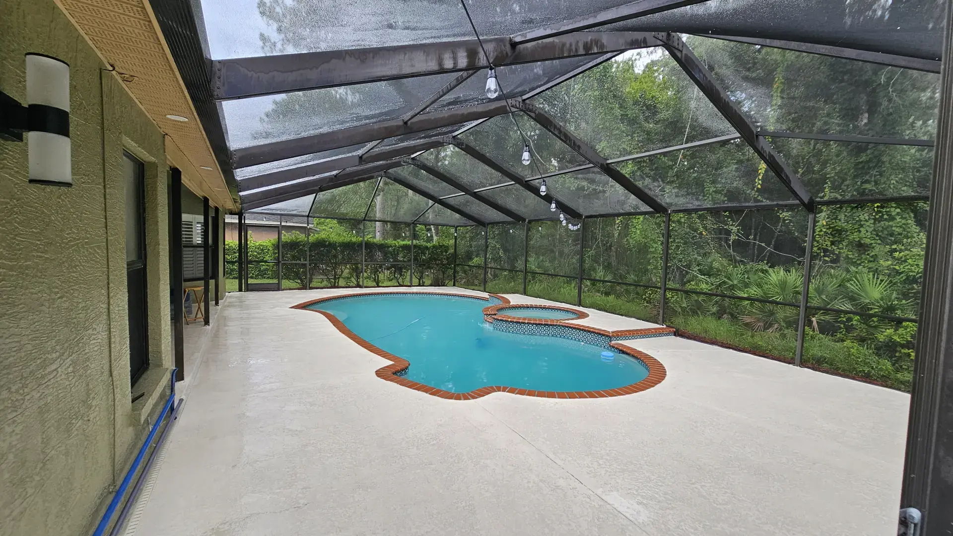 Let Us Restore Your Outdoor Living Space Screened-in backyard pool area with curved pool and attached hot tub surrounded by concrete decking and garden